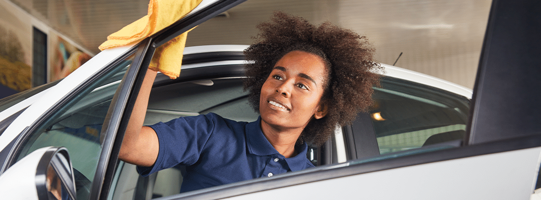 Dealership service professional cleaning car window.